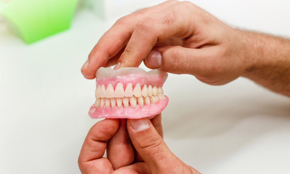 Mão a segurar prótese dentária removível total para ilustrar opções de reabilitação oral